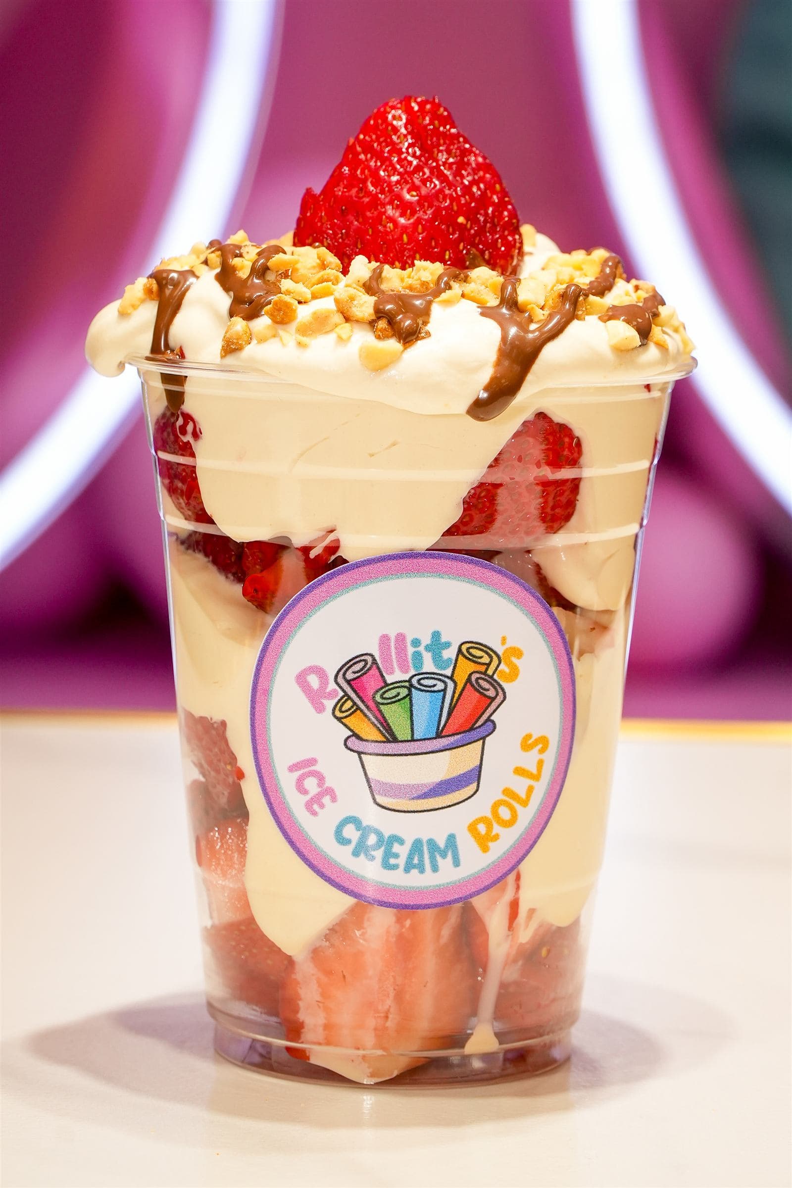 Strawberry shake cup with whipped cream, chopped peanuts, and chocolate drizzle